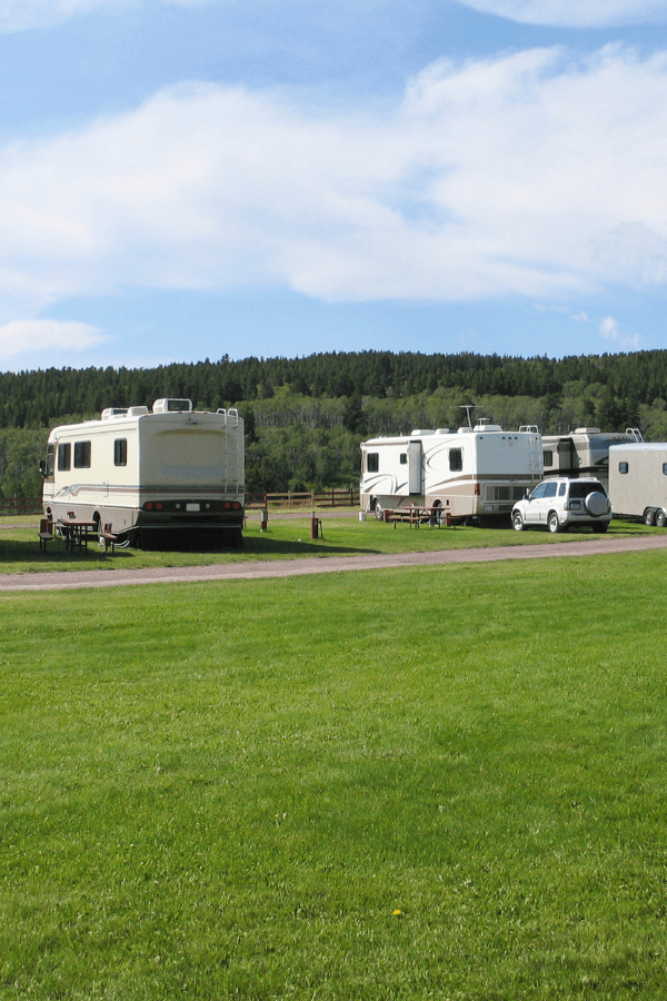 RV's parked in green field with forest in background
